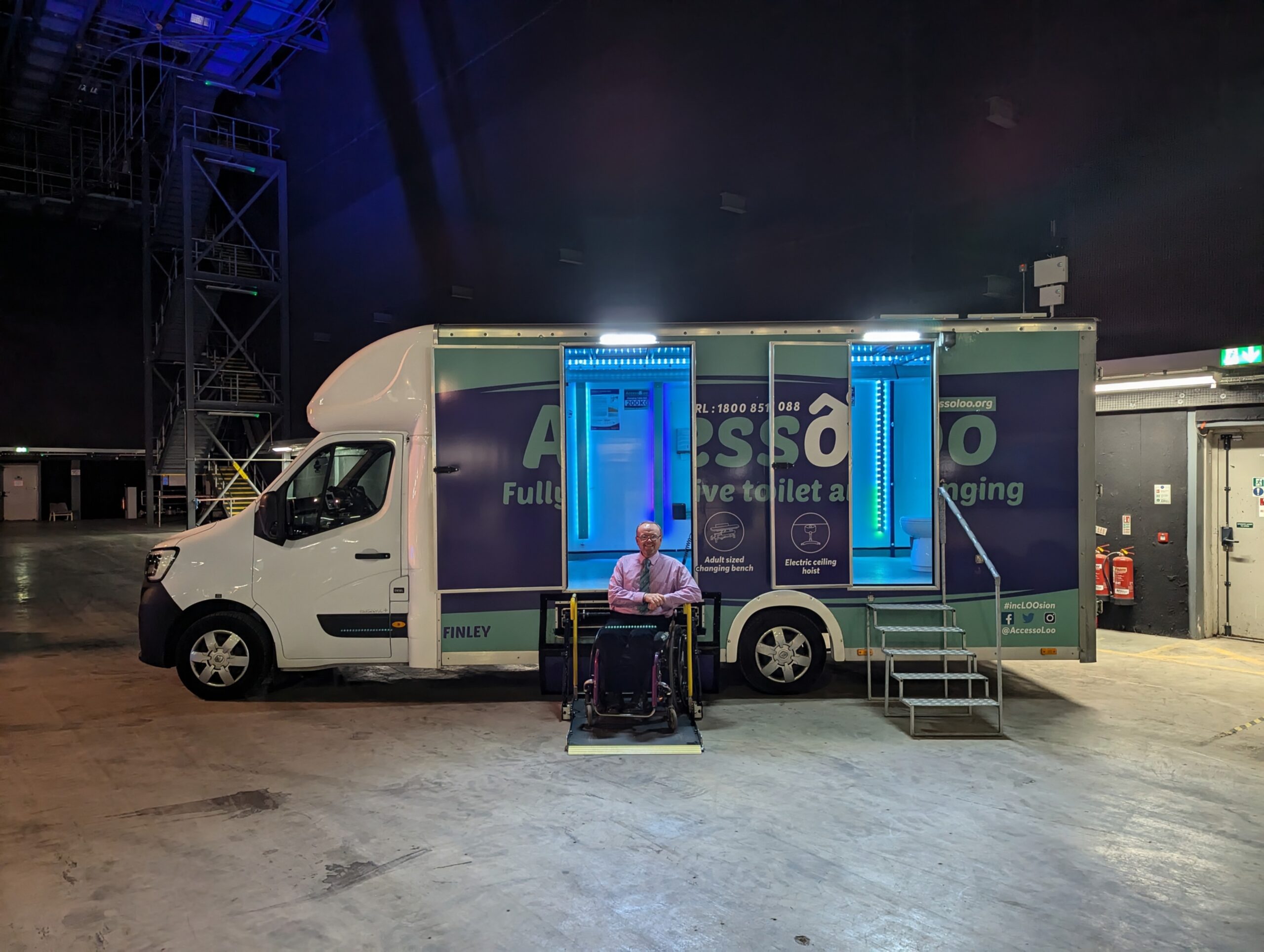 AccessoLoo Finley parked inside a film studio. Platform lift deployed with Michael sitting in his wheelchair beside it.
