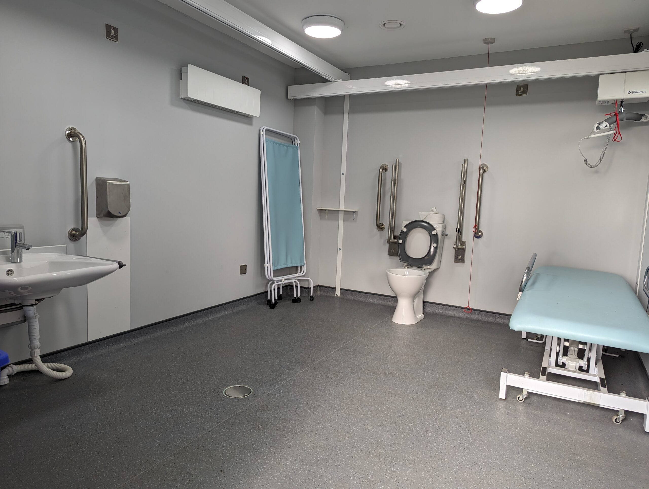 A view of inside a modular Changing Places with toilet, sink, ceiling hoist and changing table in view.